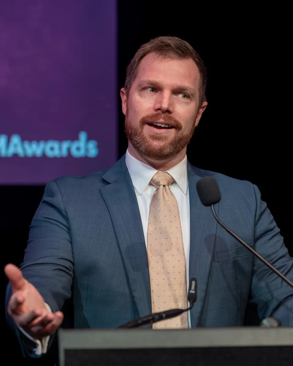 Andrew speaking at a lectern at an awards night, reaching out to the audience