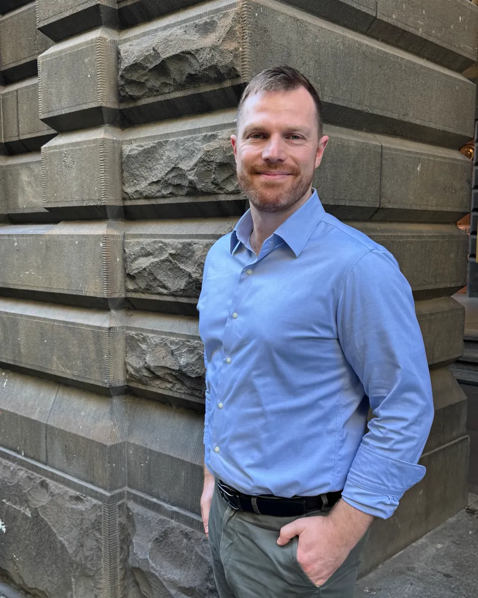 Andrew standing by a bluestone wall, smiling